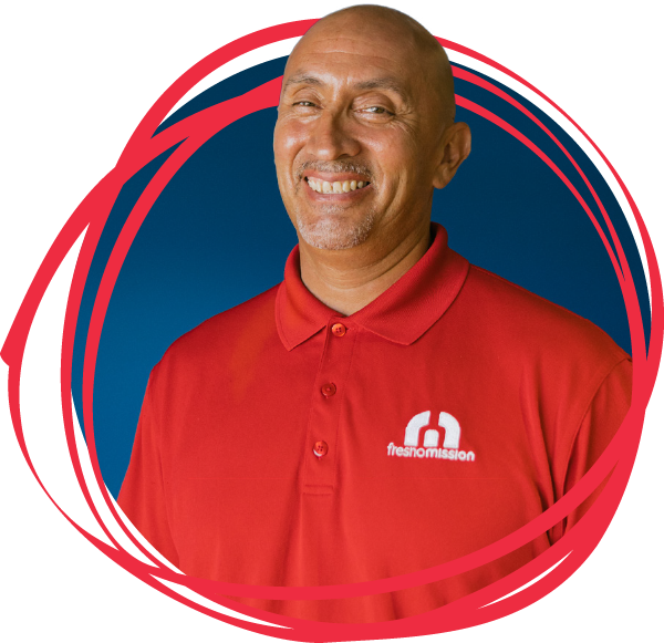 A smiling man in a red polo shirt with the freshmission logo stands in front of a blue background, framed by red graphic shapes.