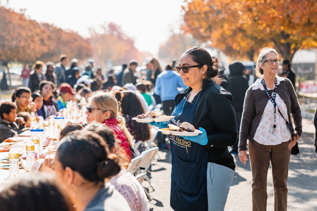 A volunteer serves plates to guests seated along the long table