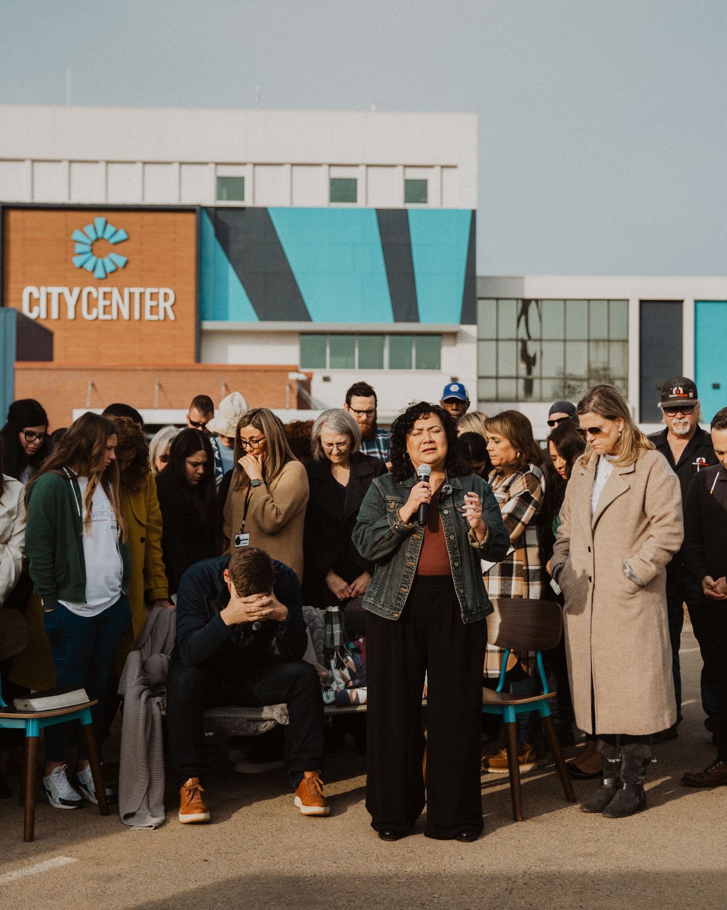A woman leads prayer with a microphone surrounded by the community